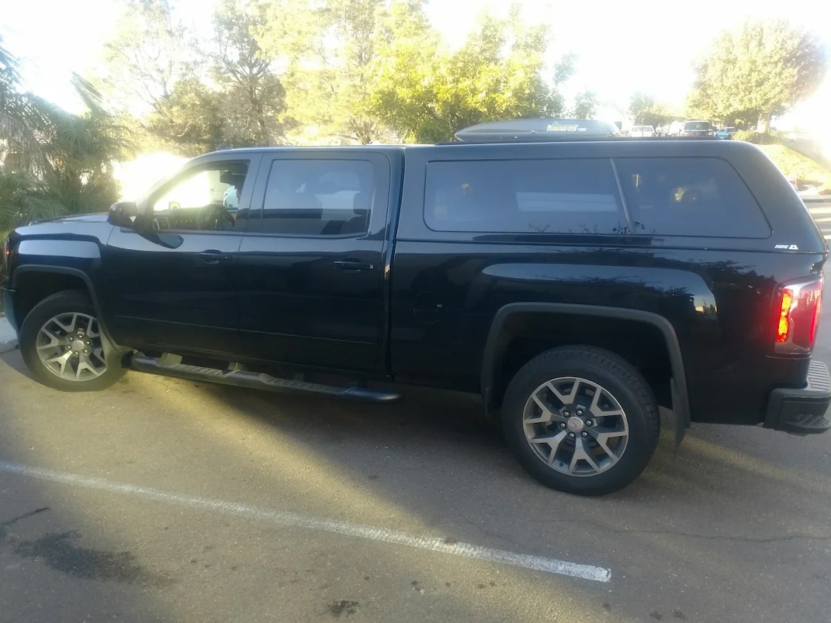 Black pickup with a color-matched truck cap, roof cargo box, and step bars