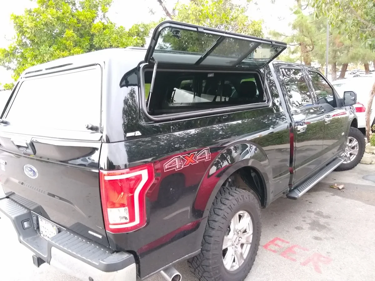Black pickup with a color-matched truck cap and its gullwing side door propped open