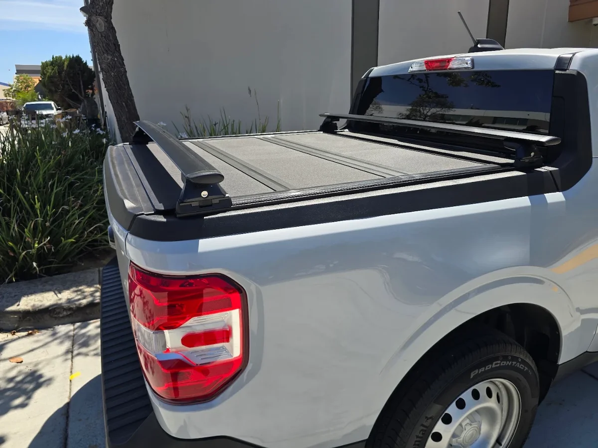 White Ford Maverick with a hard folding tonneau cover and crossbars mounted on the bed rails