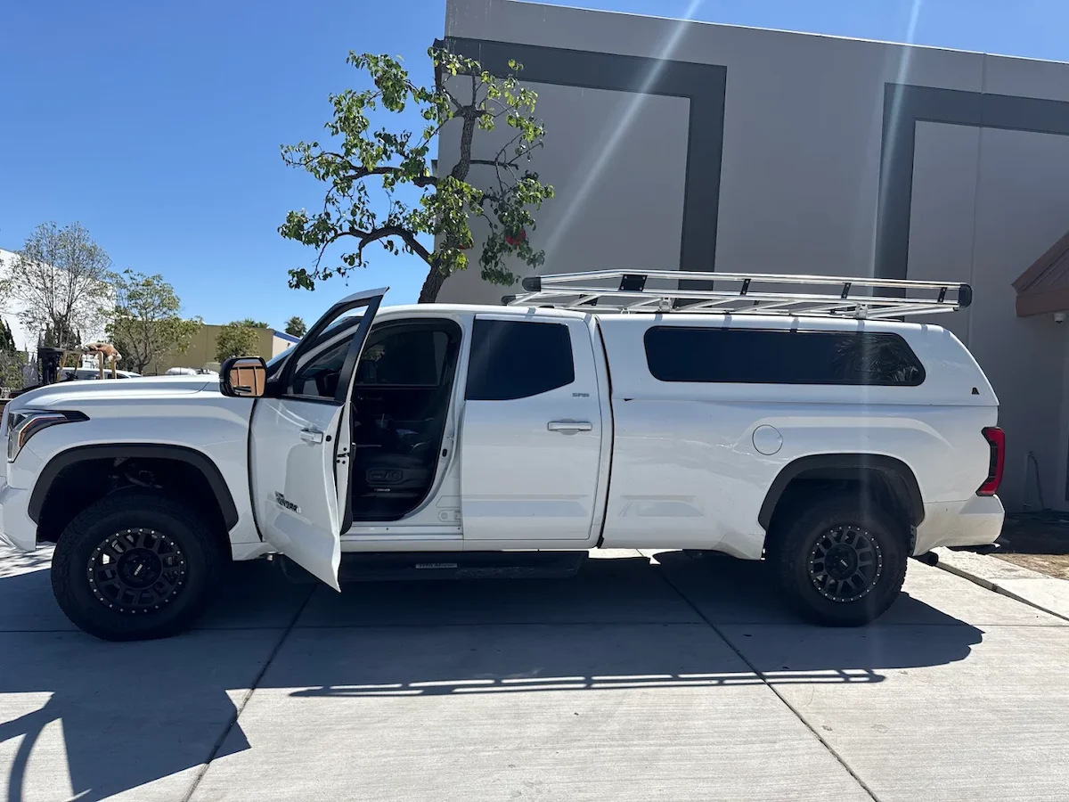 White pickup with a tall commercial truck cap and an over-cab ladder rack